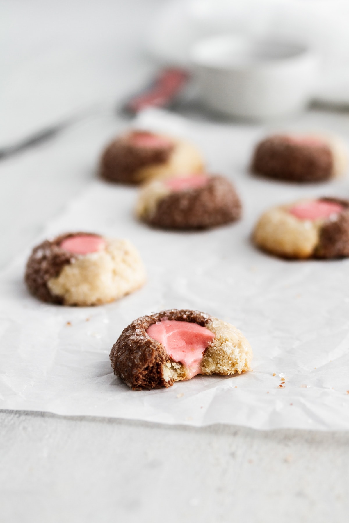Neapolitan thumbprint cookies on parchment paper with a bite taken out of one