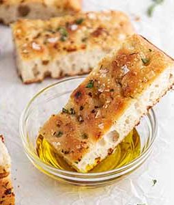 slice of sourdough focaccia dipped into a bowl of olive oil