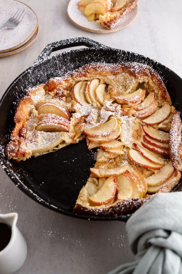 side view of German apple pancake in a cast-iron skillet with a slice taken out